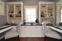 two white chairs sitting in front of a window next to bookshelves and cabinets