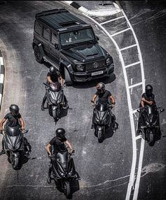 a group of bikers riding down the street in front of a black car and suv