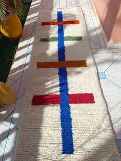 a colorful rug is on the ground next to a potted plant and yellow vases