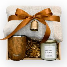 a gift box containing a candle, coffee mug, and blanket with a bell on it