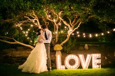 a couple standing next to each other in front of a tree with lights on it