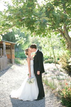 a bride and groom kissing under a tree in front of a wooden structure at the end of their wedding day