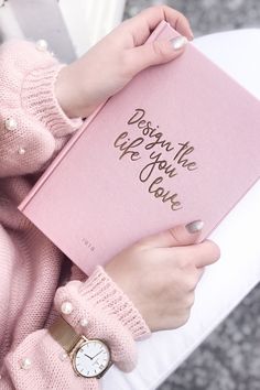 a woman holding a pink book with writing on it