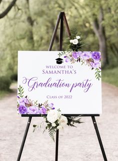 a welcome sign with purple flowers and greenery on it for a graduation party in the woods