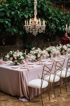 a long table is set up with pink and white flowers, candles, and chandeliers