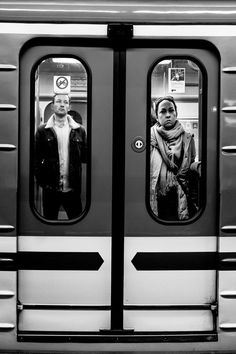 two people standing in the doorway of a subway train, with their reflection in the doors