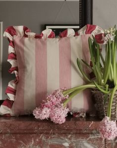 pink and white striped pillow sitting on top of a table next to a vase with flowers