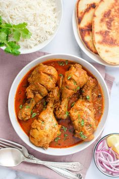 two bowls filled with chicken curry next to rice and pita bread on a table