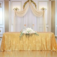 a gold table cloth with white flowers and candles on it in front of a chandelier