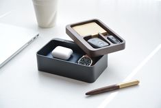 an office desk with a pen, watch and cell phone in a box next to a coffee cup