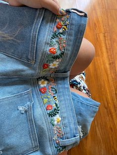 a woman is holding her jeans with flowers on them