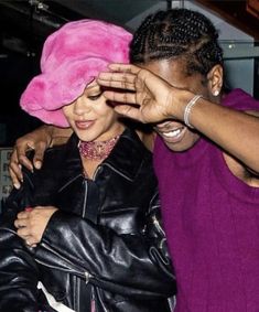 a woman covering her eyes with a pink hat on top of another woman's head