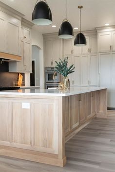 a large kitchen with white cabinets and wood flooring on the counter top, along with black pendant lights hanging from the ceiling