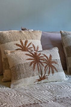 two pillows with palm trees on them sitting on a bed