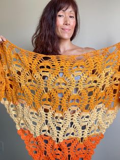 a woman holding up a crocheted shawl with oranges and browns on it