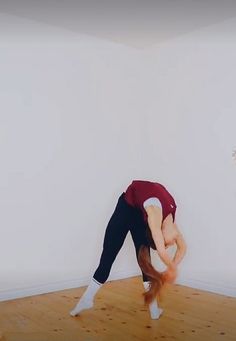 a person doing a handstand on a wooden floor in front of a white wall