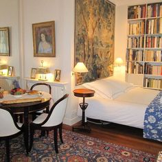 a bedroom with a bed, table and chairs in it next to a bookshelf