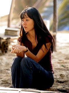 a woman sitting on the ground with her hand in her pocket and looking at something