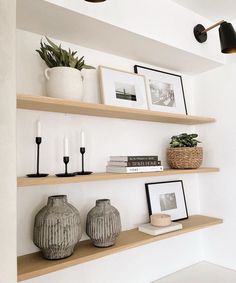 two vases are sitting on the shelves with books and pictures above them, along with other decorative items