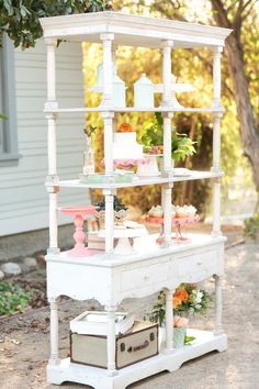 a cake stand with flowers and cakes on it in front of a white house outside