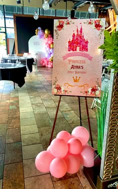 a sign that has some balloons on it in front of a table with chairs and tables