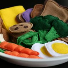 an egg, carrots and other felt items in a bowl