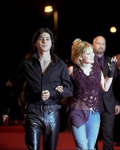 two people walking down a red carpet with one person wearing black and the other in purple