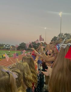 a group of people standing on top of a field with american flags in their hands