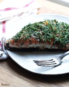 a piece of salmon covered in herbs on a plate with a fork next to it