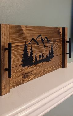 a wooden sign with mountains and trees on the front is hanging from a mantel