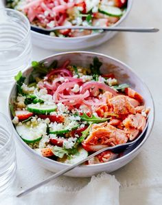 two white bowls filled with food on top of a table next to water glasses and spoons