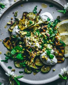 a white plate topped with zucchini and other vegetables next to lemon wedges