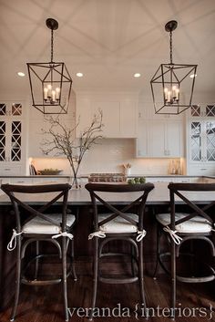 a kitchen with two chandeliers hanging from the ceiling and four chairs at the table