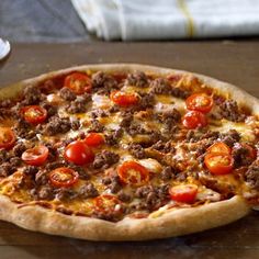 a pizza sitting on top of a wooden table covered in cheese and tomato toppings