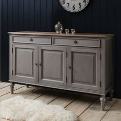 a large clock is on the wall above a gray cabinet with two doors and drawers