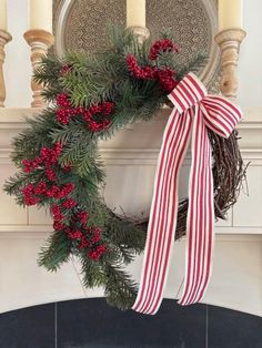 a christmas wreath with red berries and greenery hanging from the front of a fireplace