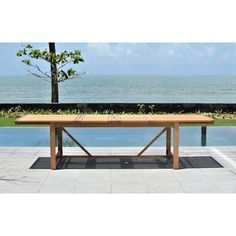 a wooden table sitting on top of a cement floor next to a swimming pool with the ocean in the background