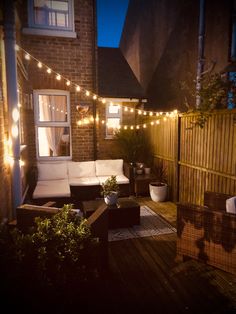 a patio with lights strung over it and furniture on the deck outside at night time