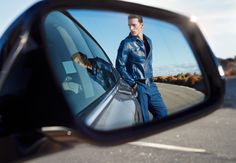 a man standing next to a car looking in the side mirror