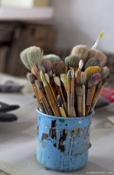 a blue bucket filled with lots of different types of paintbrushes on top of a table