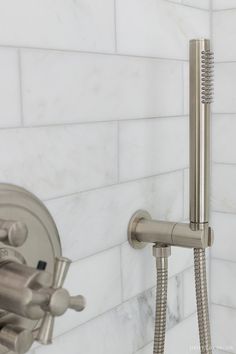 a faucet and shower head in a white tiled bathroom with marble tiles on the walls