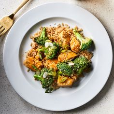 a white plate topped with chicken and broccoli covered in sauce next to a fork