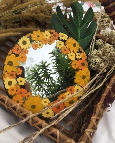 a mirror sitting on top of a table next to dried grass and flowers in a basket