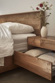 a bed with white sheets and pillows next to a wooden headboard that has drawers underneath it