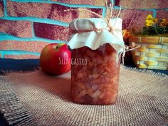 a jar filled with red onions sitting on top of a table next to an apple