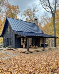 a small blue cabin in the woods surrounded by leaves and trees with fall foliage on the ground