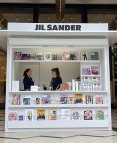 two women are standing in front of a book store with shelves full of books and magazines