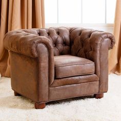 a brown chair sitting in front of a window next to a white rug and tan curtains