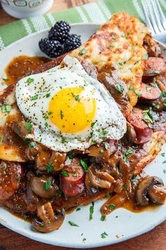 a white plate topped with hash browns and an egg on top of it next to blackberries