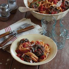 pasta with meatballs and tomato sauce in a bowl on a wooden table next to empty glasses